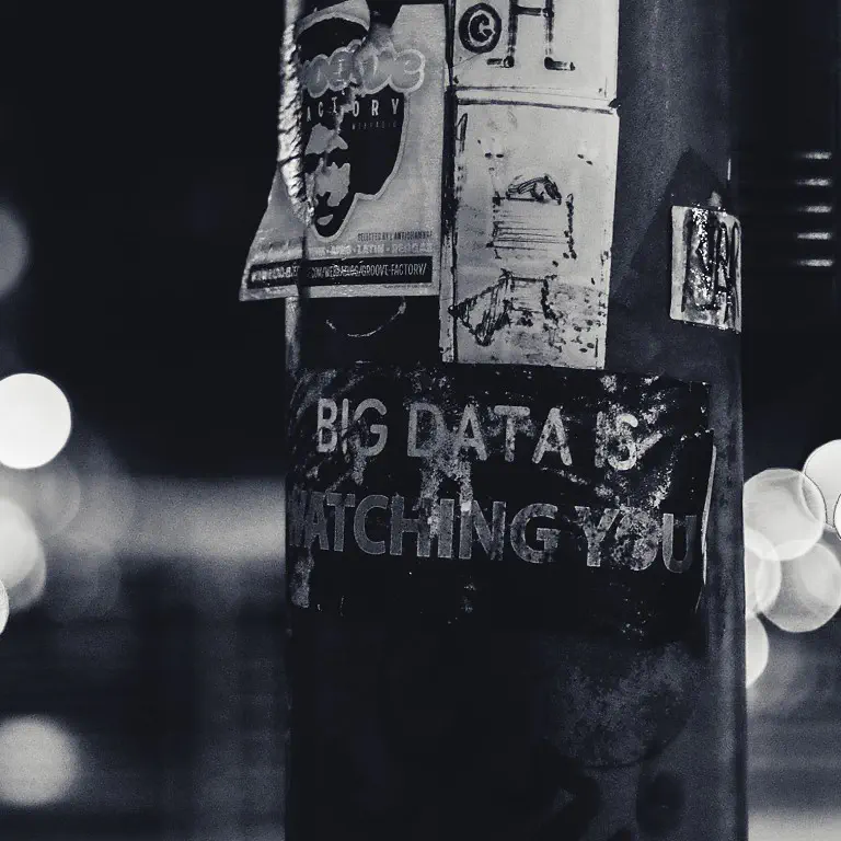 Big data is watching you A dark photo of a pole with the words 'Big data is watching you' stuck to it.